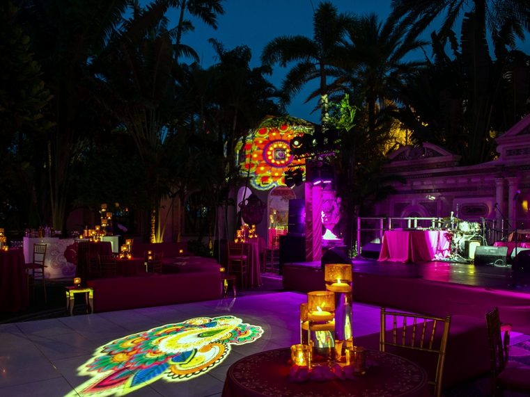 The same courtyard at night, with a projected pattern on the dance floor, candlelit tables, and a lit stage