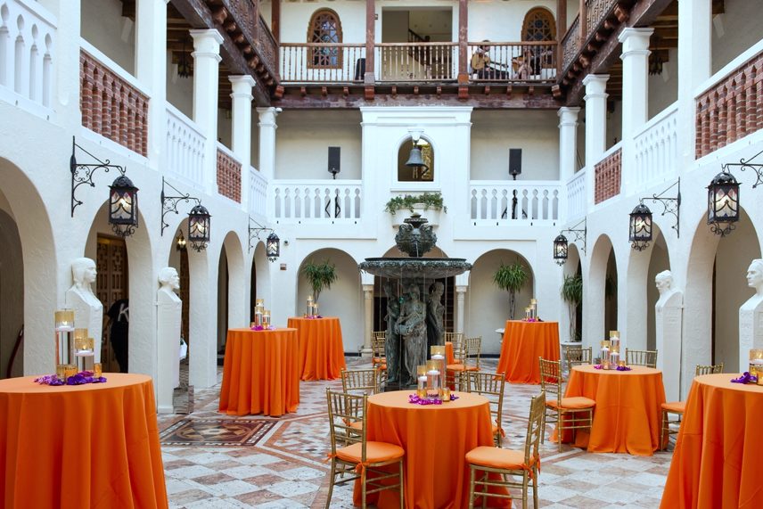 Welcome reception in an arched courtyard with orange linens and lanterns